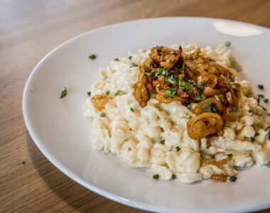 Echte Allgäuer Kässpätzle mit geschmolzenem Käse und Röstzwiebeln auf weißem Teller im Restaurant Hotel zur Rose.